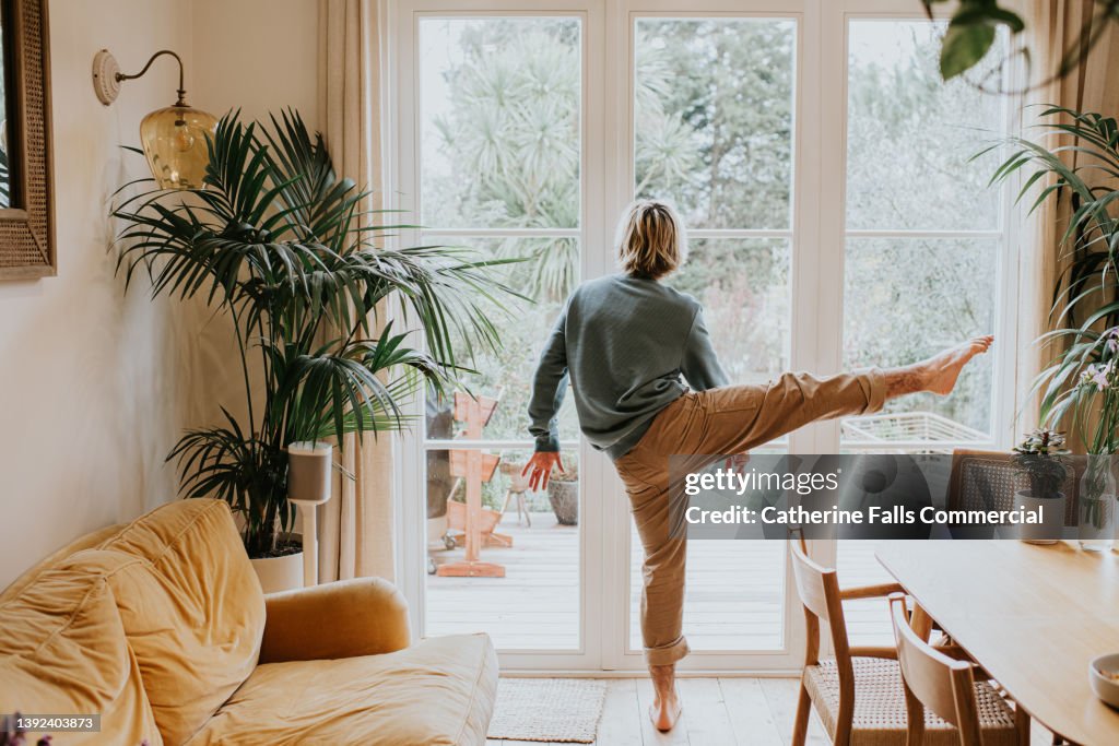 A flexible man stretches / dances in front of large patio doors in a stylish home environment