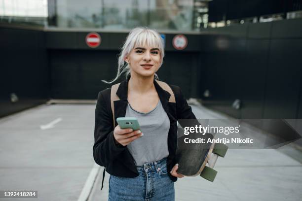 portrait of a female commuter holding mobile and skateboard - women skateboarding stock pictures, royalty-free photos & images