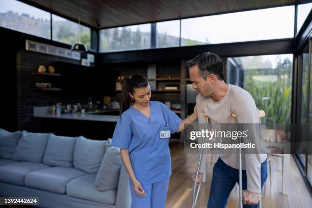 injured man walking on crutches at home with the help of his nurse - man walking feet inside stock pictures, royalty-free photos & images