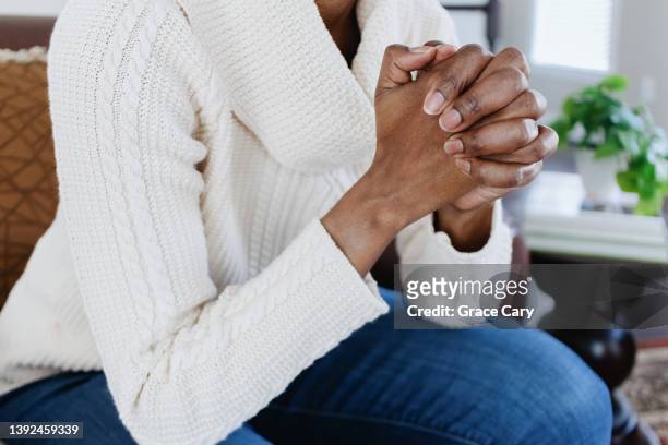 woman sits in chair with hands clasped - women prayer stock-fotos und bilder