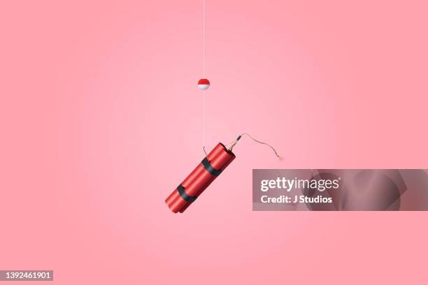 conceptual image of dynamite stick on a fish hook - explosive stock pictures, royalty-free photos & images