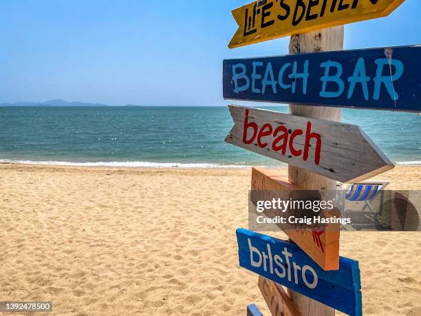 colourful thai beach sign with arrows to the beach, bistro, bar and emotions such as relaxation, chill and enjoy. fun sign post billboard in the sand with beach and sea view on horizon. concept piece for family holiday, beach and vacation marketing - beach sign stock pictures, royalty-free photos & images