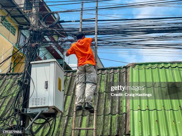 thai engineer fixing repairing a mess of hanging cables at a local power communication hub exchange. despite the disorder and health and safety risks thailand continues to have some of the fastest broadband in the world - 6g stock pictures, royalty-free photos & images