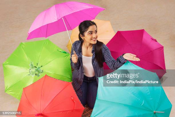 portrait of a young girl kneeling with surrounded with multicolored umbrellas - enjoy monsoon stock-fotos und bilder