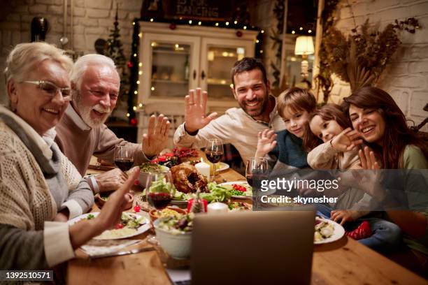 happy extended family greeting someone on video call during dinner at dining table. - virtual lunch stock pictures, royalty-free photos & images