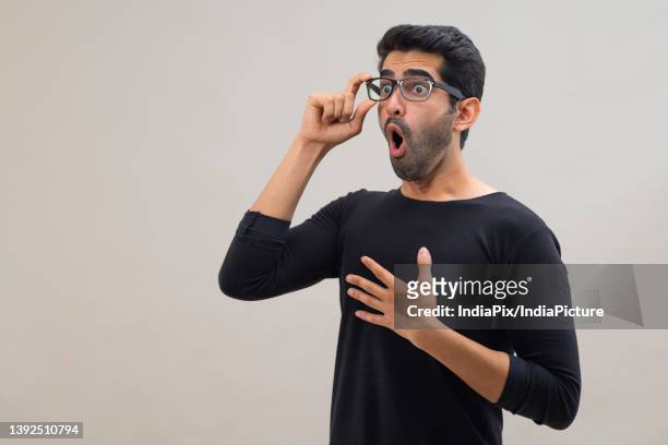 portrait of a stunned young man looking elsewhere with open mouth, wide eyes and hands on his chest - hands on chest stock pictures, royalty-free photos & images