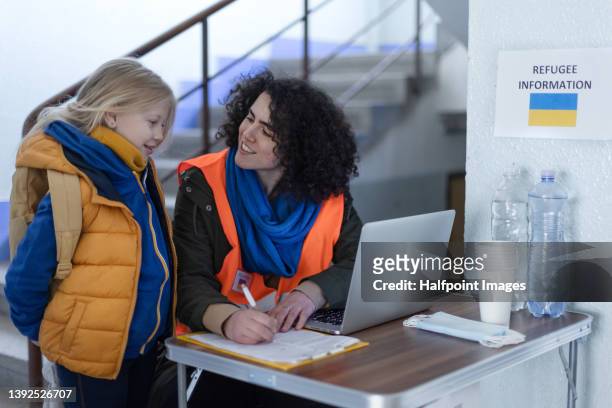 volunteer giving information to ukrainian refugee child at train station. - zivilist stock-fotos und bilder