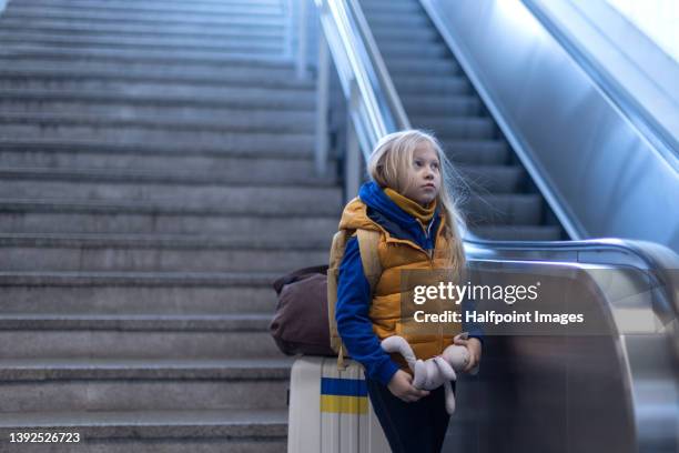 sad ukrainian immigrant child with luggage waiting at train station, ukrainian war concept. - refugees stockfoto's en -beelden