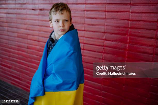 boy wearing ukrainian flag against red brick wall. - ukraine war stockfoto's en -beelden