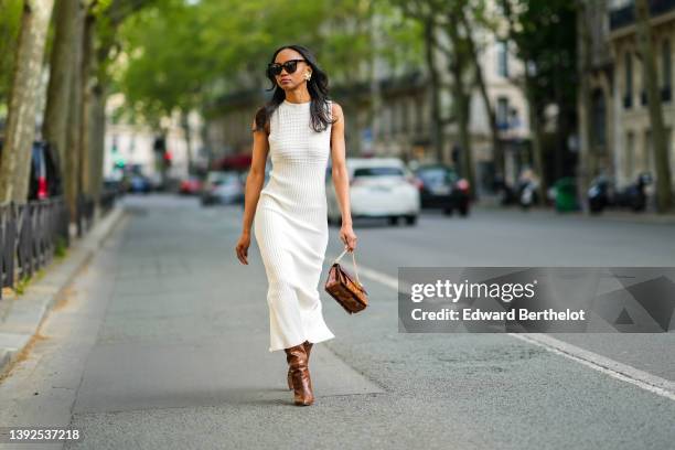 Emilie Joseph @in_fashionwetrust wears black sunglasses, large gold vintage earrings, a white embossed checkered pattern high neck / sleeveless /...
