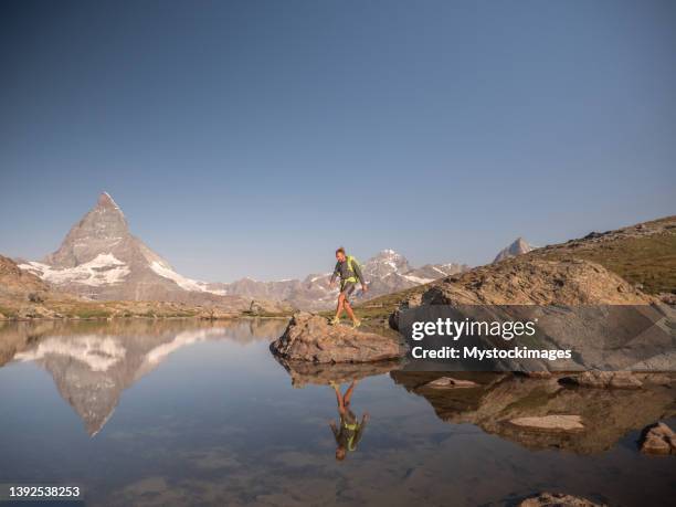 man jumps from rock to rock on alpine lake - zermatt stock pictures, royalty-free photos & images