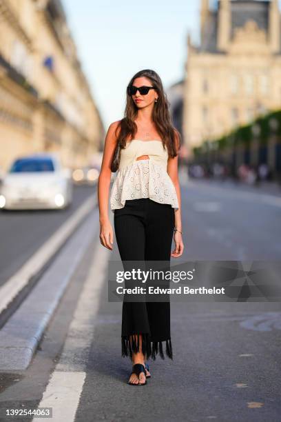 Amanda Derhy wears black sunglasses, gold and rhinestones pendant earrings from Dior, a gold chain pendant necklace, a white latte braided...
