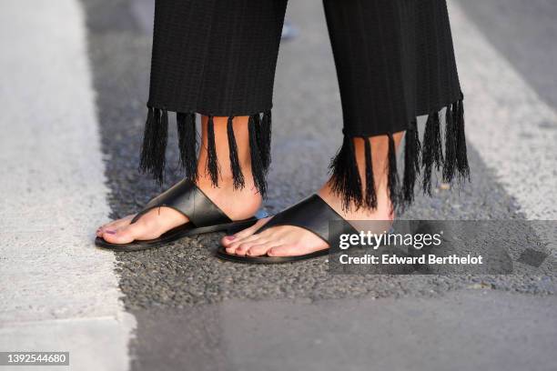 Amanda Derhy wears black fringed wide legs pants, black shiny leather flip-flop / shoes, during a street style fashion photo session, on April 17,...