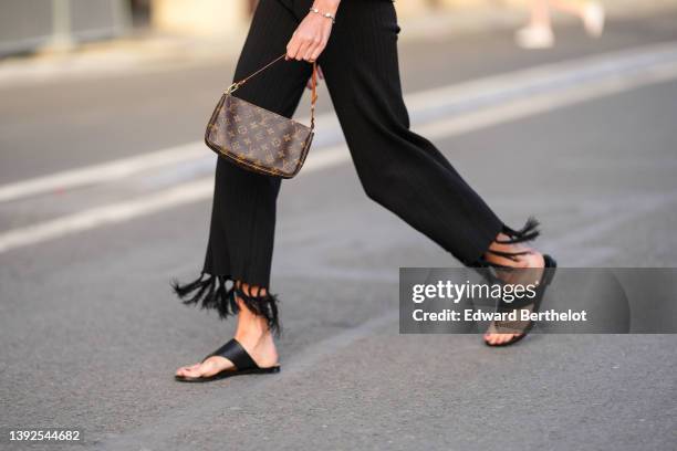 Amanda Derhy wears a brown shiny monogram print pattern in coated canvas shoulder bag from Louis Vuitton, black fringed wide legs pants, black shiny...