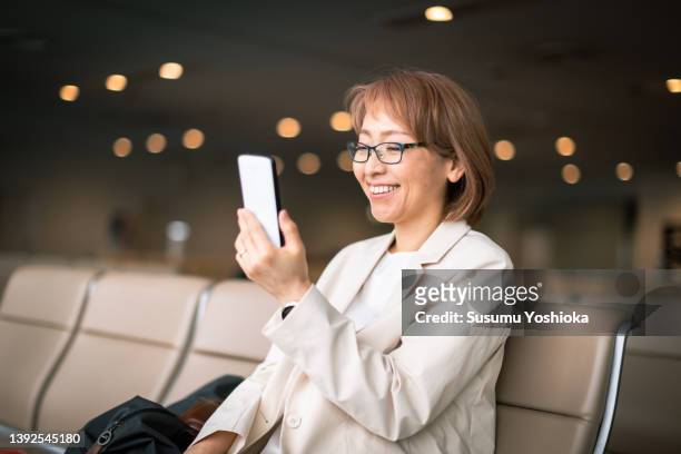 businesswoman working on a bench in an airport lobby - business smartphone happy spring fotografías e imágenes de stock