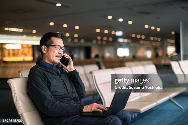 businessman working on a bench in an airport lobby - abrigo negro fotografías e imágenes de stock