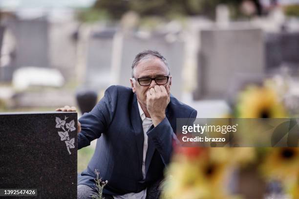 mann mittleren alters vor gräbern auf einem friedhof - mourning stock-fotos und bilder