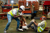 African American factory worker having accident while working in manufacturing site while his colleague is asking for first aid emergency team using walkie talkie radio for safety workplace concept