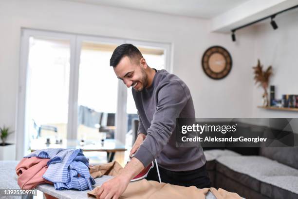 hispanic male ironing pile of clothing at home - ironing board imagens e fotografias de stock