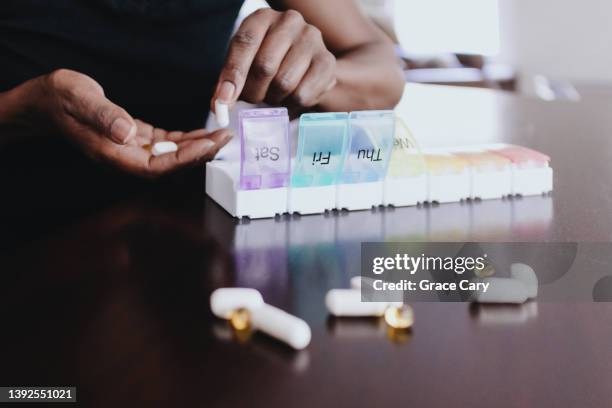 woman organizes her daily dose of pills/supplements with multicolored pill container - magnesium - fotografias e filmes do acervo