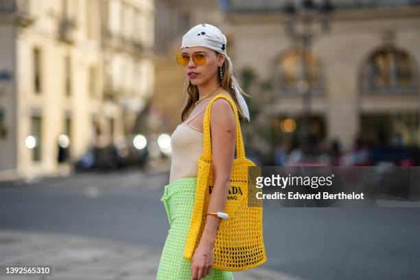 Almuneda Lapique wears a white with black print pattern silk scarf as a headband, yellow sunglasses, green sunglasses, a silver large chain necklace,...