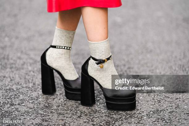 Gabriella Berdugo wears a high waist red shiny leather midi skirt, gray socks, black shiny satin block heels pumps heels shoes from Versace with...