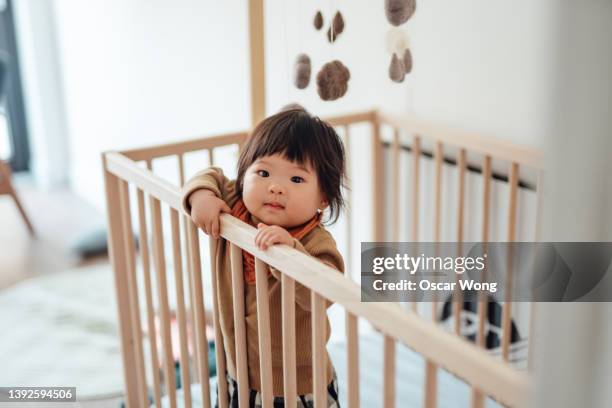 smiling asian baby girl standing in cot - baby girl stock pictures, royalty-free photos & images
