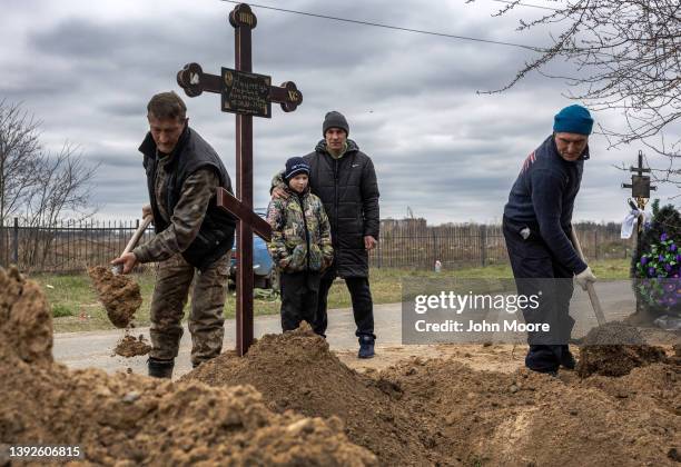 Grave diggers shovel soil into the grave of a woman as her husband and son watch on April 20, 2022 in Bucha, Ukraine. Hundreds of Ukrainians killed...