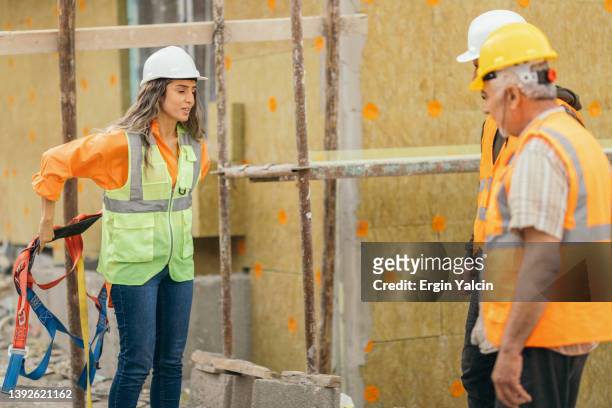female occupational safety specialist explaining  to construction site workers how to use  safety harness - metal workshop stockfoto's en -beelden