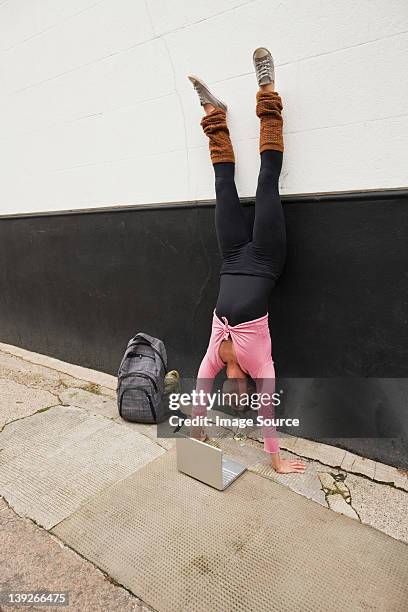 woman performing handstand and using laptop on pavement - flexible work stock-fotos und bilder