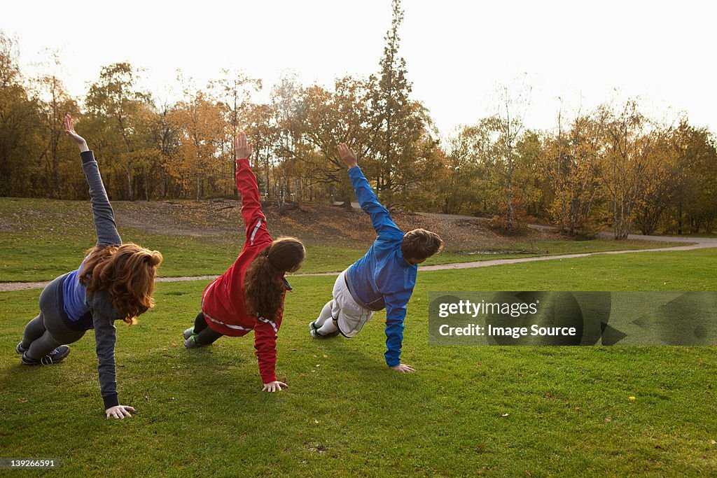 Three young friends stretching on grass in park