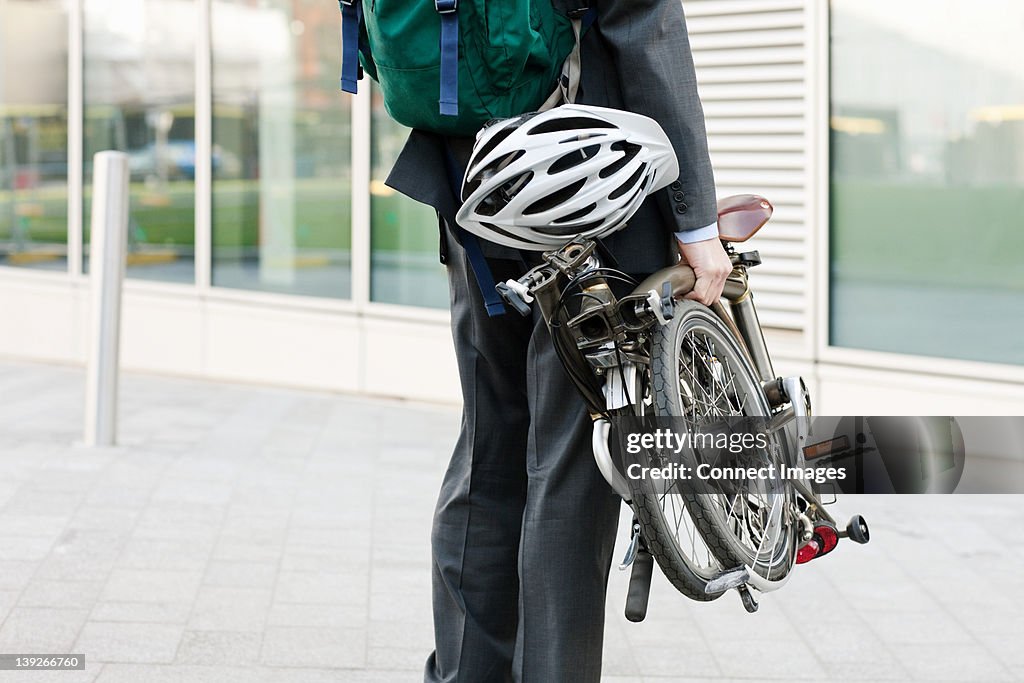 Mid adult businessman carrying folding bicycle