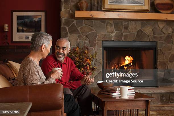 mature couple sitting by fireplace - sitting by fireplace stock pictures, royalty-free photos & images