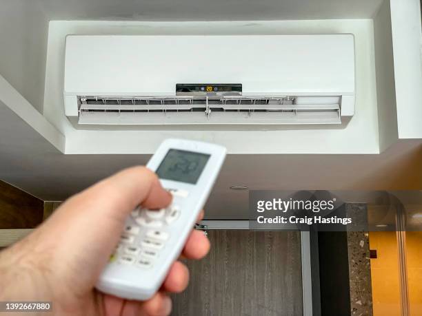 mans hand raised and pointed at air conditioning unit performing the on and off switch function in luxury hotel tourist resort. - air conditioner interior wall stock pictures, royalty-free photos & images