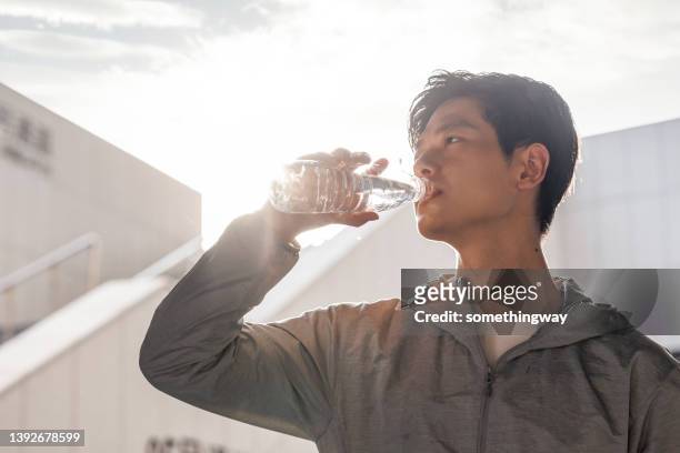 asiatische junge männer trinken nach dem training wasser im sonnenlicht - mann wasser trinken sport stock-fotos und bilder