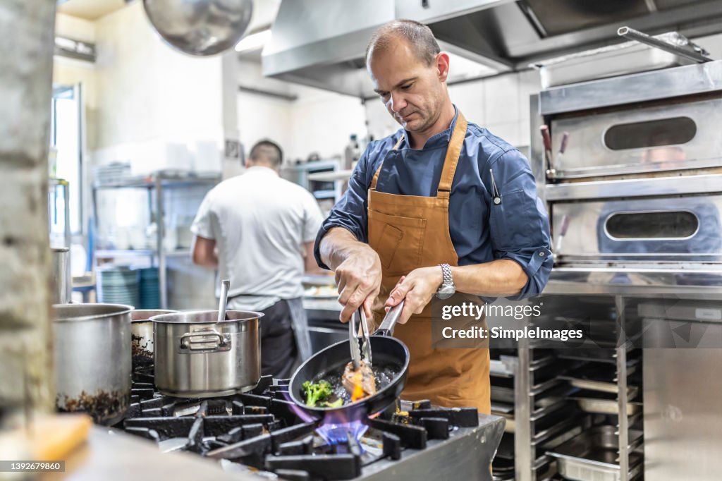 Professional chef cooks steak with fresh wegetable in the restaurant on pan.