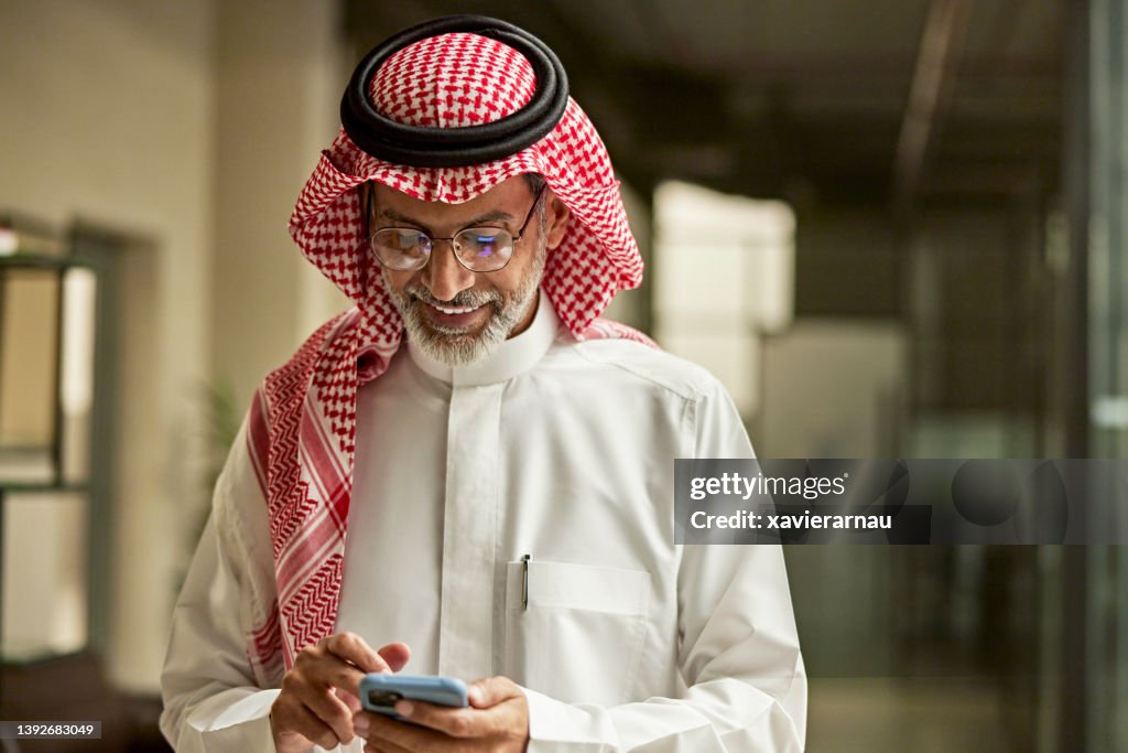 Smiling Saudi businessman checking smart phone in office
