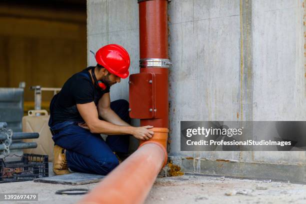 a young plumber is fixing a water pipe at a building site. - riool stockfoto's en -beelden