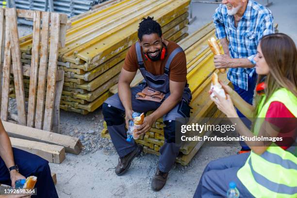 multikulturelle gruppe von bauarbeitern ruhen sich aus und erfrischen sich mit essen und trinken. - mittagspause stock-fotos und bilder