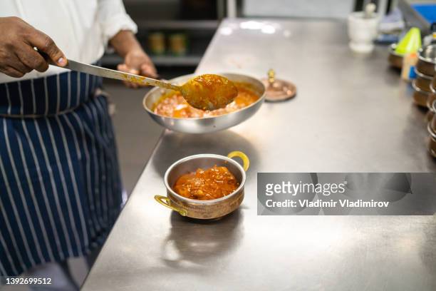 a curry dish being placed into a serving bowl - sudderen stockfoto's en -beelden