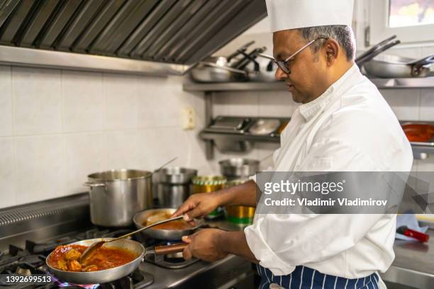a professional cook stirring food in a frying pan - sudderen stockfoto's en -beelden