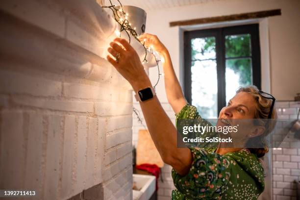 putting up string lights in her home - hanging 個照片及圖片檔