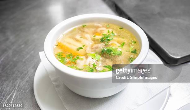 strong chicken broth in a white bowl on a stainless steel table in a restaurant kitchen. - hühnersuppe stock-fotos und bilder