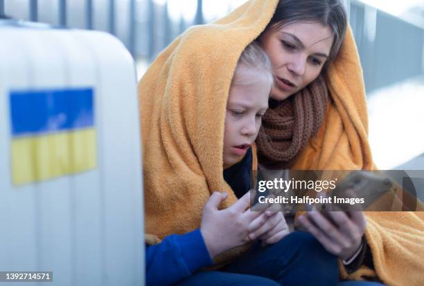 ukrainian immigrants mother with daughter with luggage waiting at train station and having video call. - crisis ストックフォトと画像