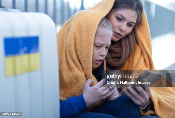 ukrainian immigrants mother with daughter with luggage waiting at train station and having video call. - refugee crisis stockfoto's en -beelden