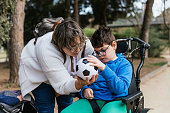Child with multiple disabilities in a wheelchair playing with a soccer ball with her mother outdoors.