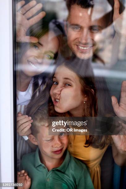 portrait of happy family behind windowpane - quetschen stock-fotos und bilder