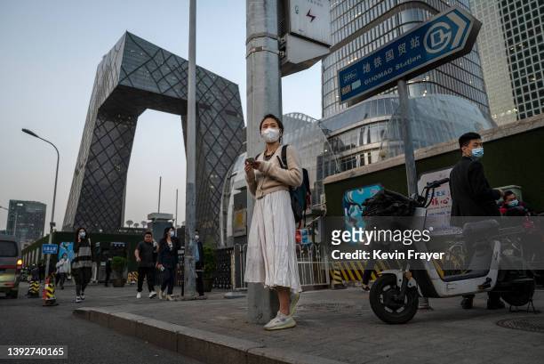 Woman looks at her mobile phone as she waits for a bus during evening rush hour in the Central Business District on April 21, 2022 in Beijing, China.