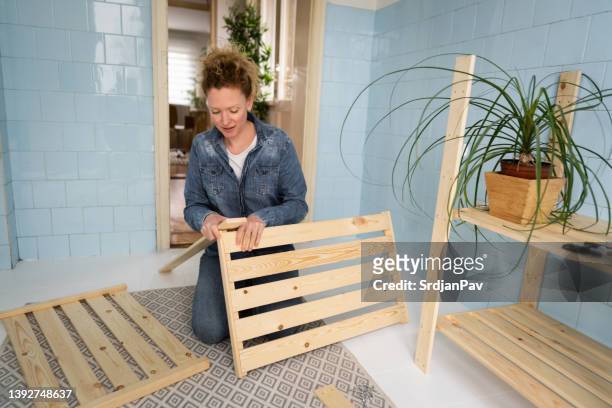 woman assembling the wooden shelf in her kitchen - building shelves stock pictures, royalty-free photos & images