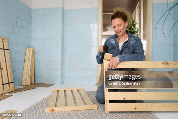 woman using electric screwdriver to assemble the wooden shelf in her kitchen - electric screwdriver stock pictures, royalty-free photos & images
